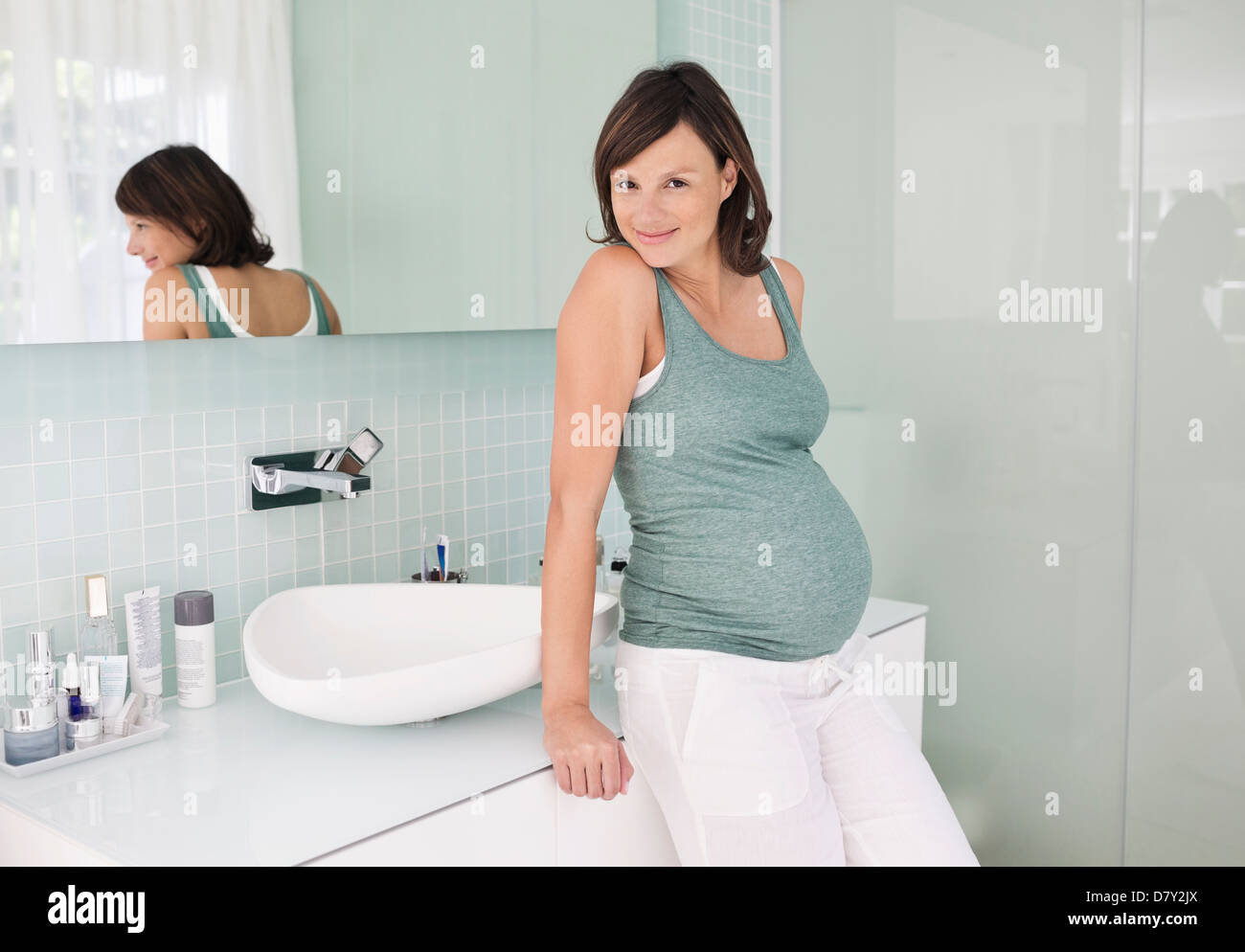 Pregnant woman leaning on bathroom sink Stock Photo