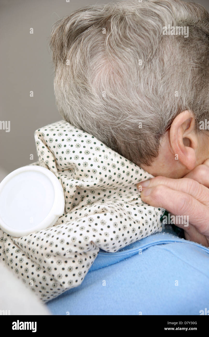 Elderly woman using a hot water bottle for neck & shoulder pain Stock Photo