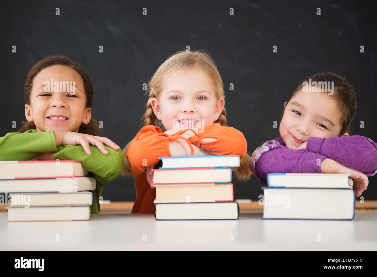 Girls leaning on stacks of books in classroom Stock Photo