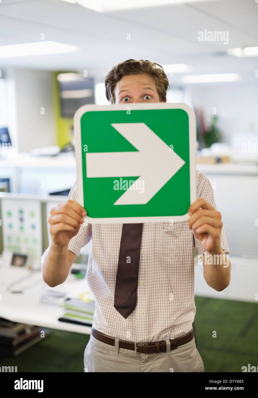 Businessman holding arrow sign in office Stock Photo