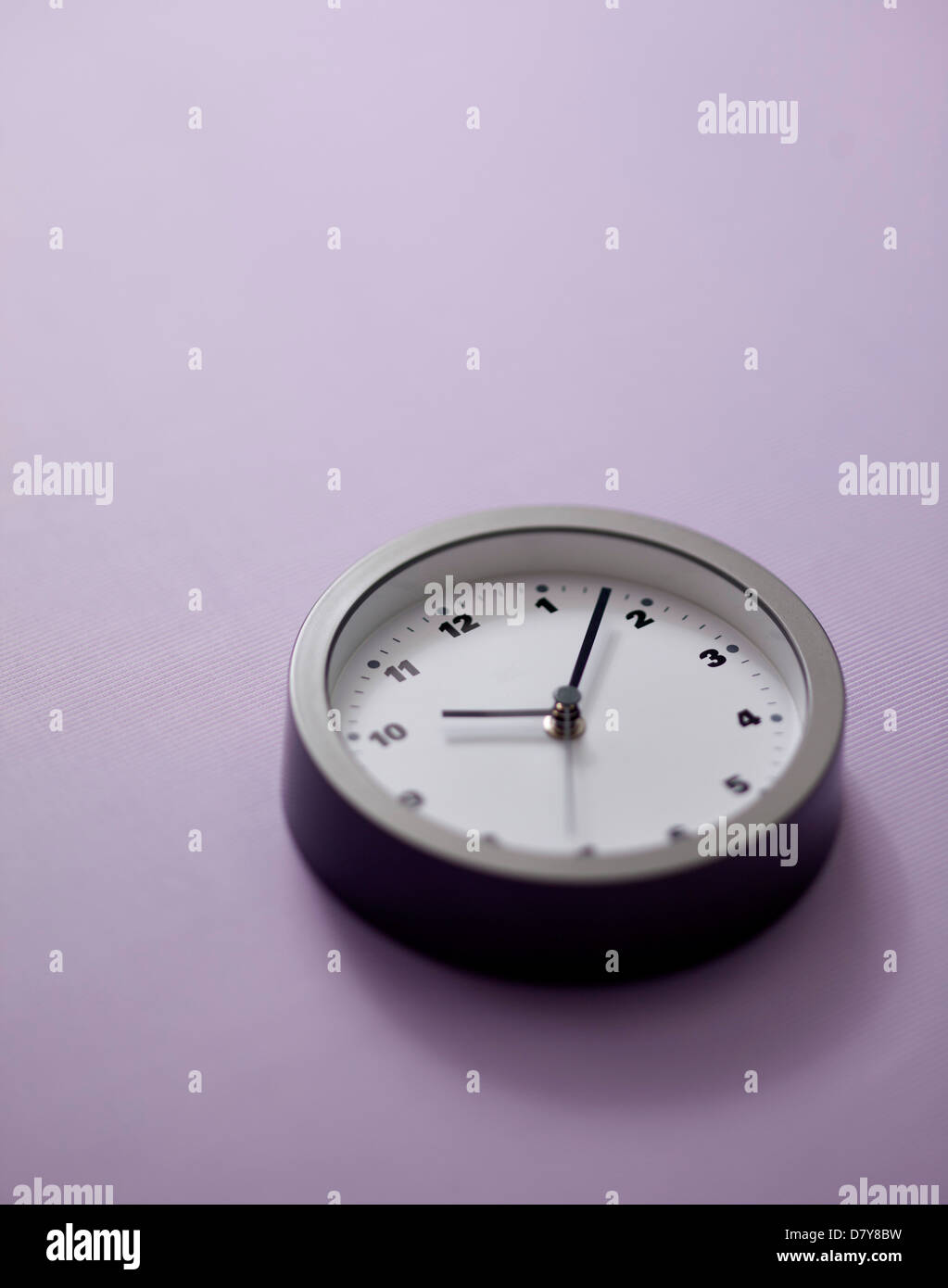 A small wall clock on a light purple wall. Stock Photo