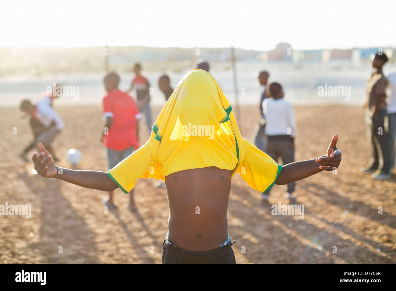 Boy celebrating with soccer jersey on his head in dirt field Stock Photo
