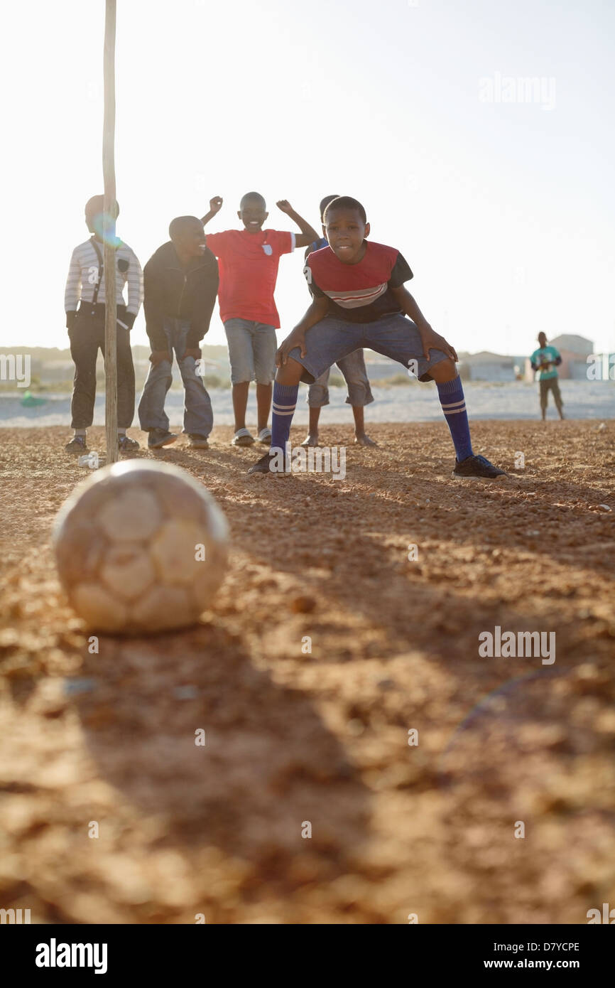 Boys playing soccer together in dirt field Stock Photo