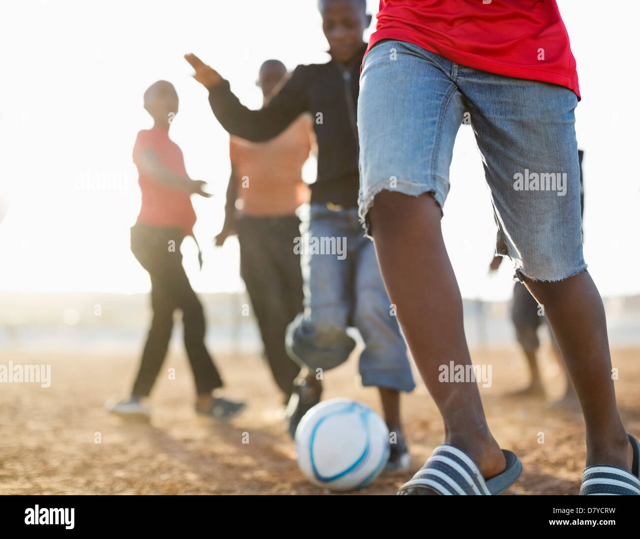 Boys playing soccer together in dirt field Stock Photo
