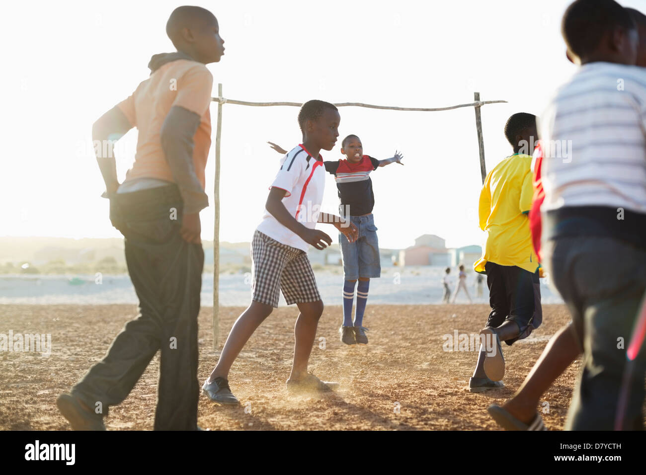 Boys playing soccer together in dirt field Stock Photo