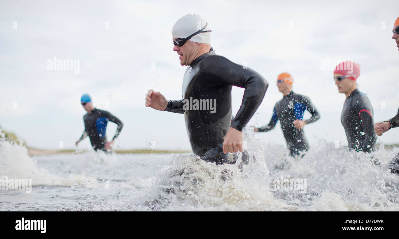 Triathletes in wetsuits running in waves Stock Photo