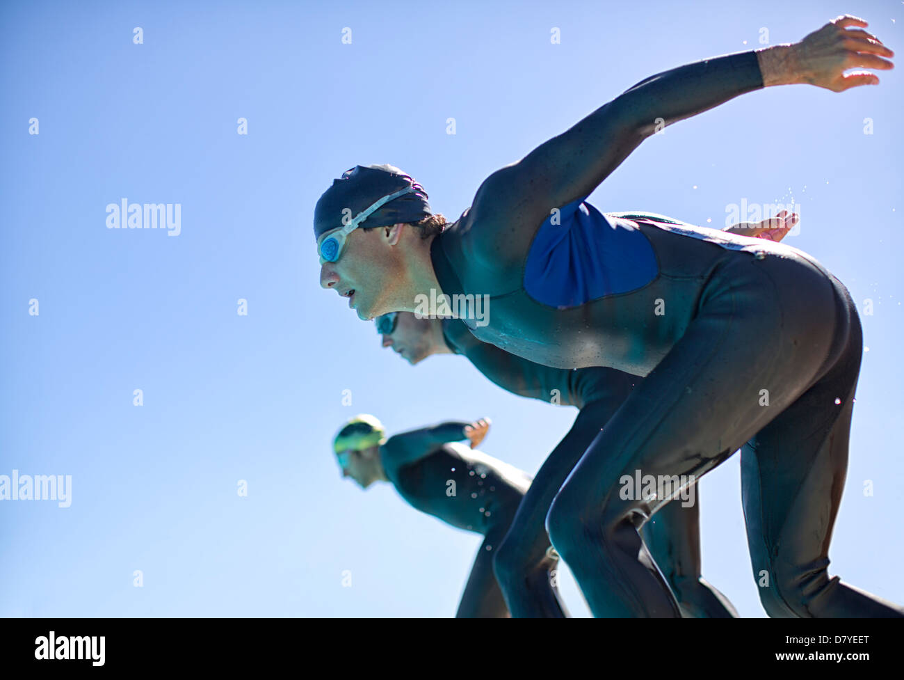 Triathletes diving into water outdoors Stock Photo