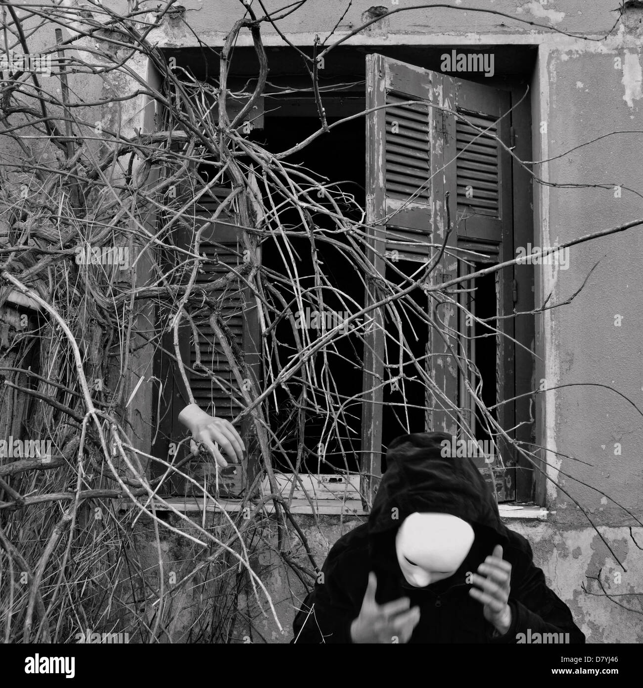 Masked figure in black and overgrown dead plants. Black and white, motion blur. Stock Photo
