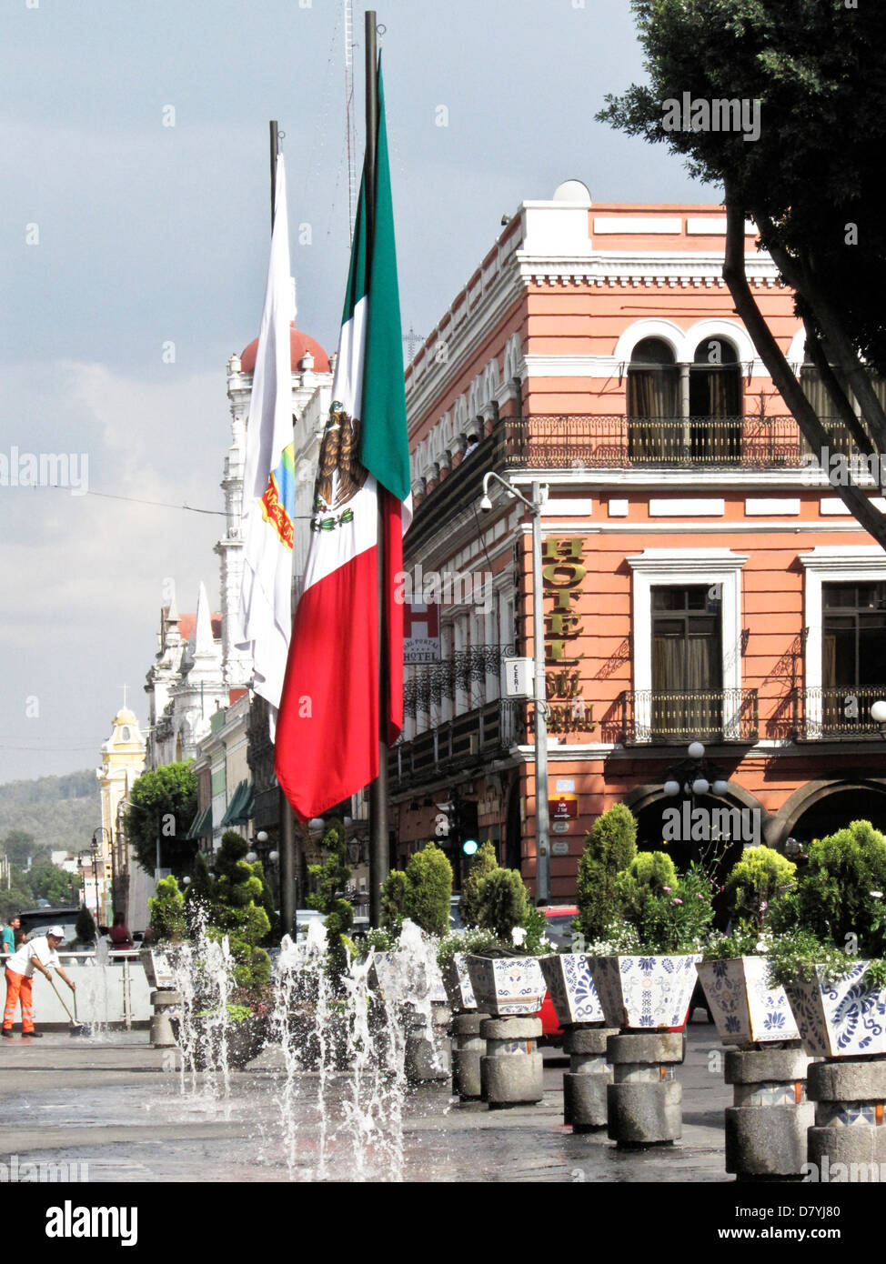 Mexican flag on post outside Palacio Municipal above play area with water jet fountains defined by shrubs atop traffic bollards Stock Photo