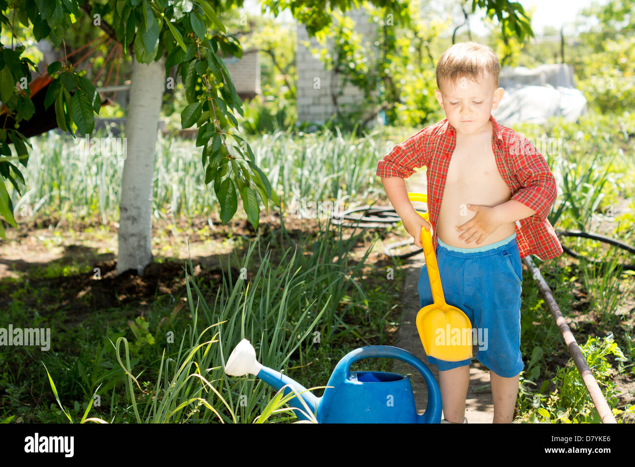 Little boy with a colourful yellow plastic toy spade in the garden ...