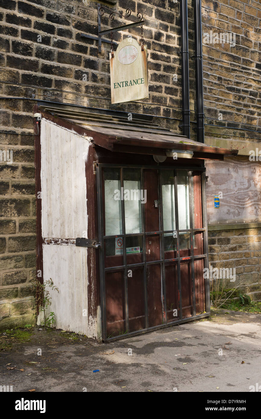 Hanging sign over dilapidated entrance to closed business (locked & bolted wooden doors) - Greenholme Mills Trading Estate, near Ilkley, England, UK. Stock Photo