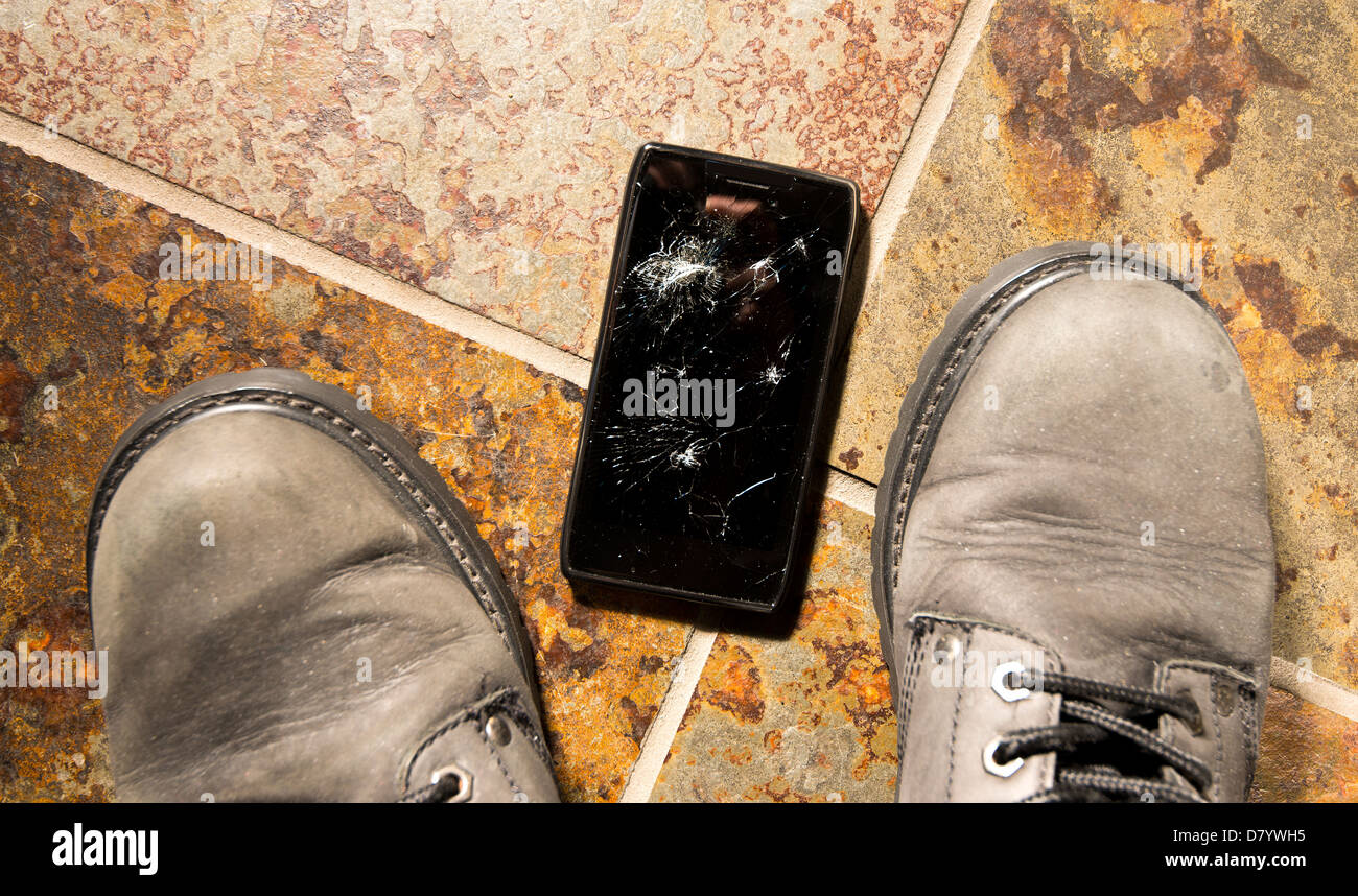 A smartphone lies broken between the workboots of its owner just after being dropped. Stock Photo