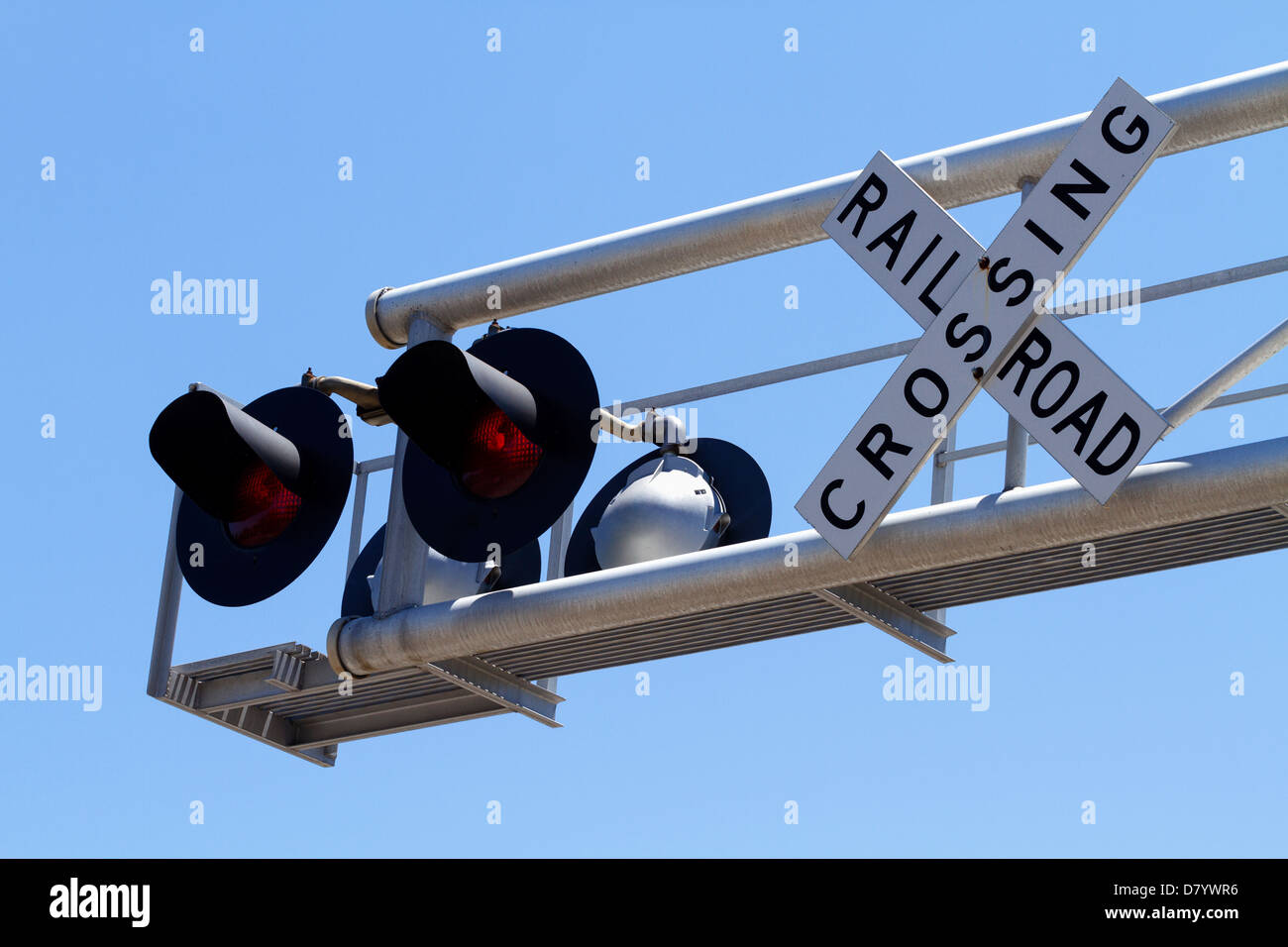 A pair of railroad crossing signal lights and railroad crossing buck sign on an overhead metal cantilever on a clear day. Stock Photo