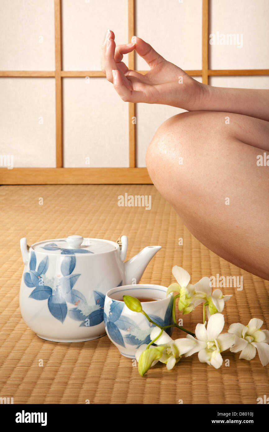 Meditating woman on japanese tatami mat with orchids and green tea Stock Photo
