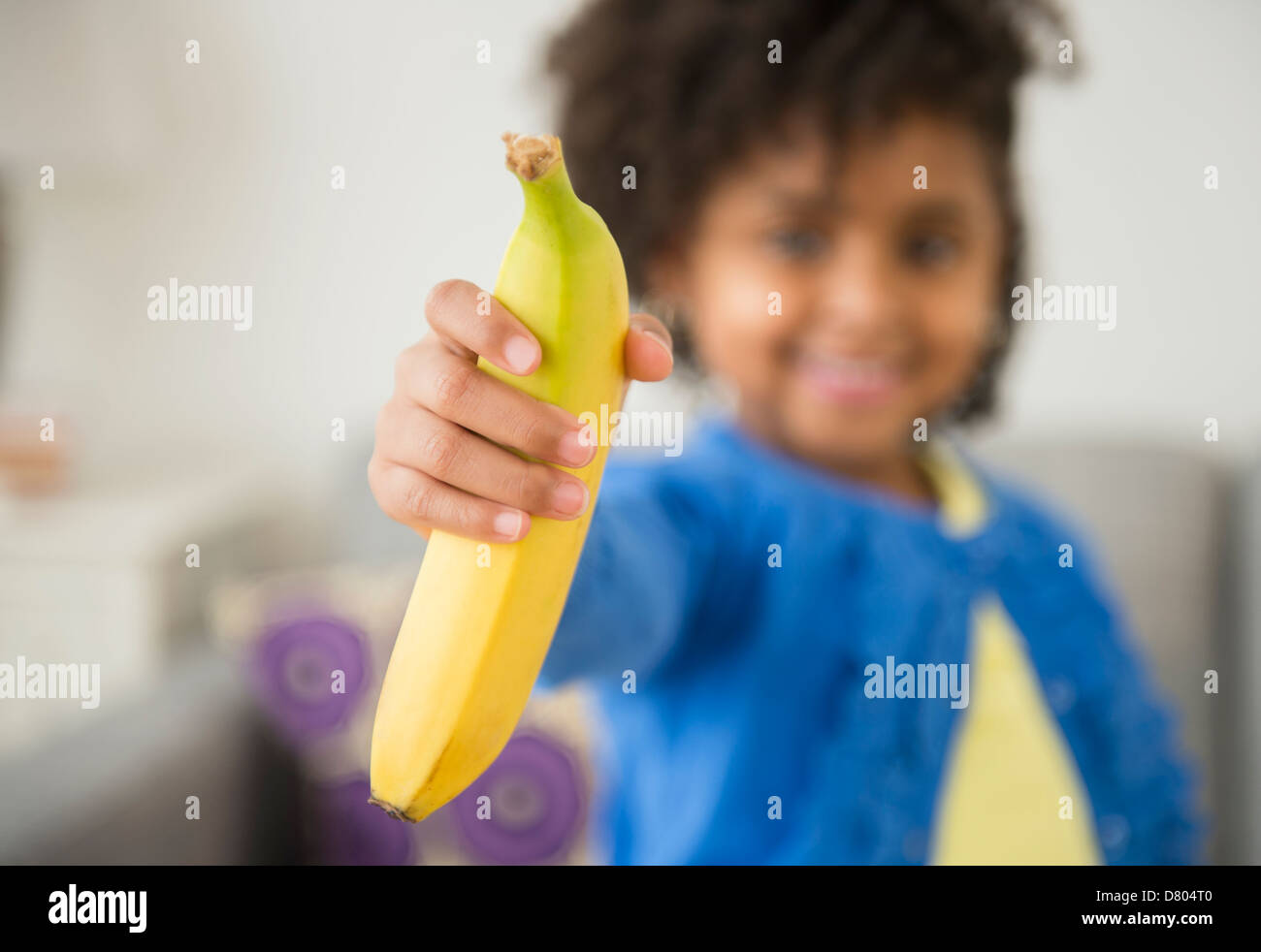 African American girl holding banana on sofa Stock Photo