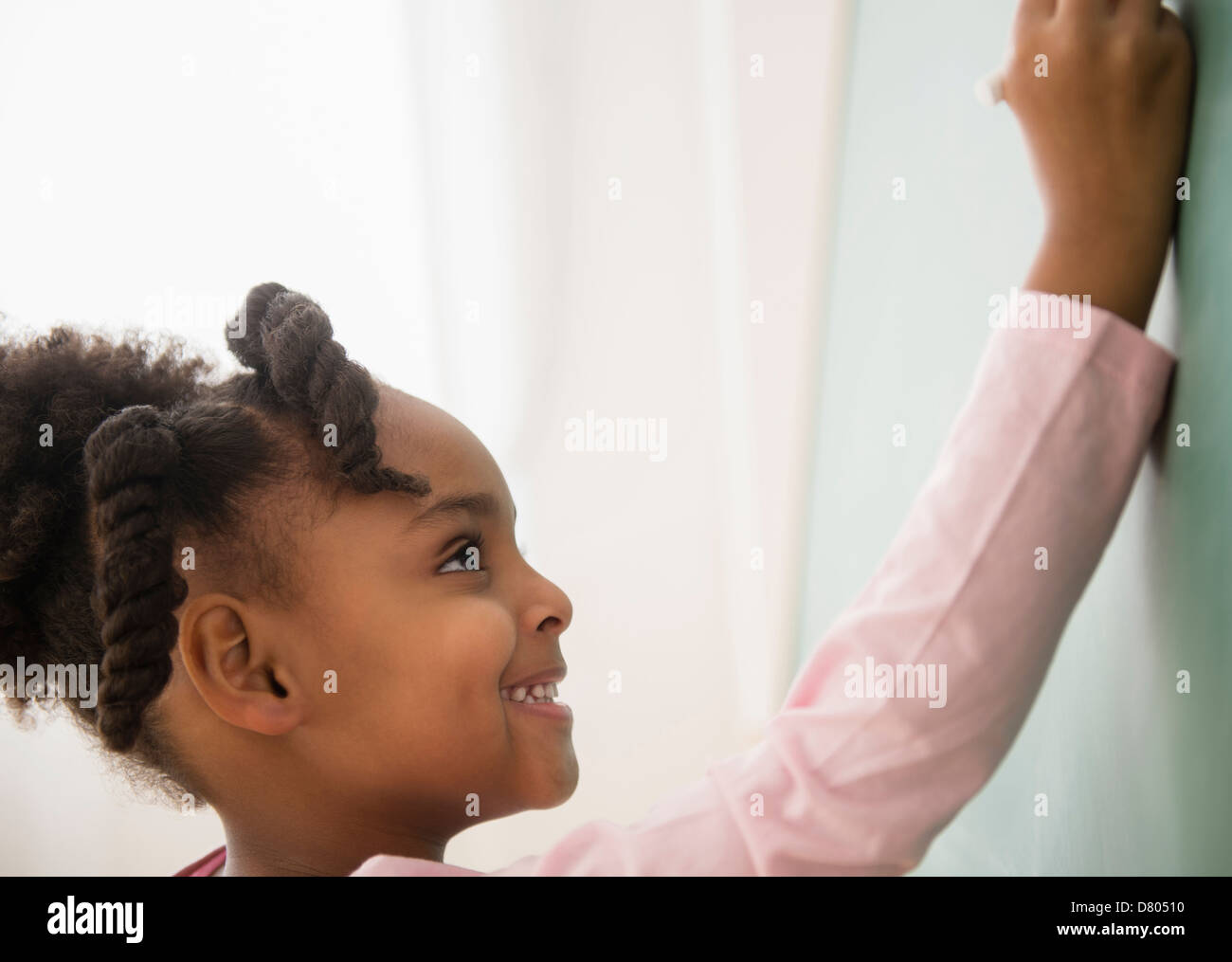 African American girl writing on chalkboard Stock Photo