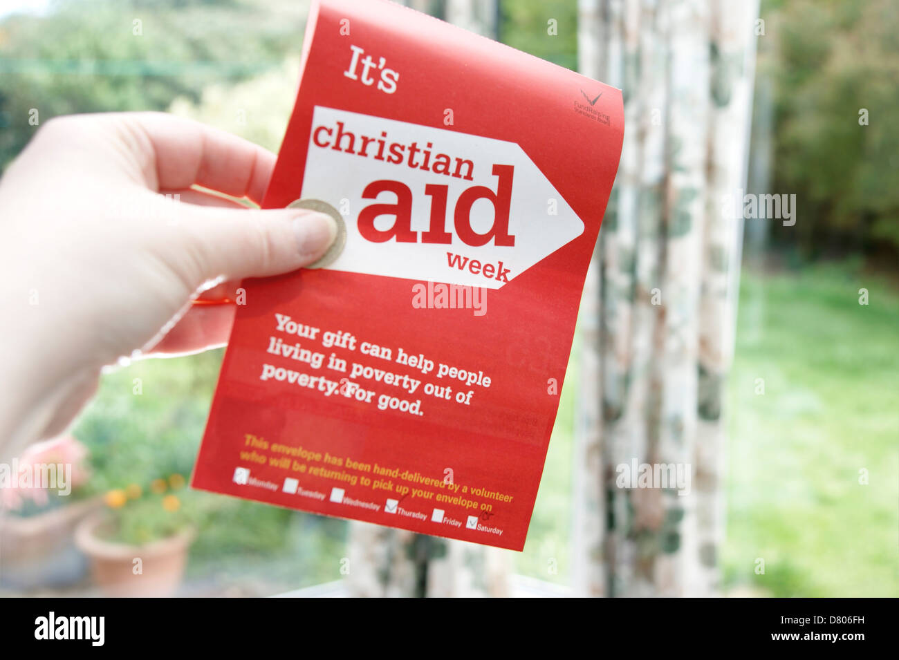 Woman holding donation of a £1 coin for a charity collecting envelope for Christian Aid week   May 2013 Stock Photo