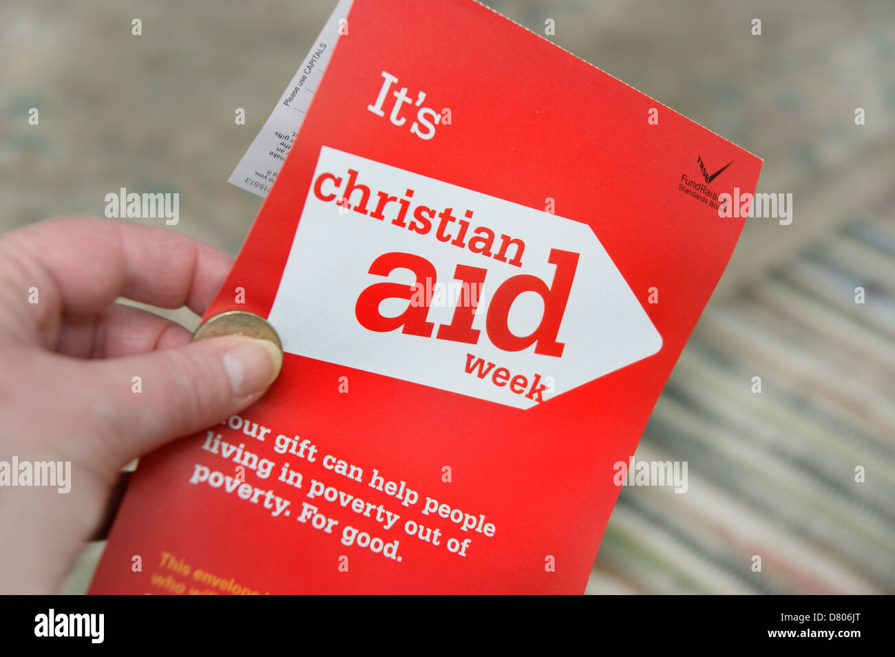 Woman holding donation of a £1 coin for a charity collecting envelope for Christian Aid week   May 2013 Stock Photo