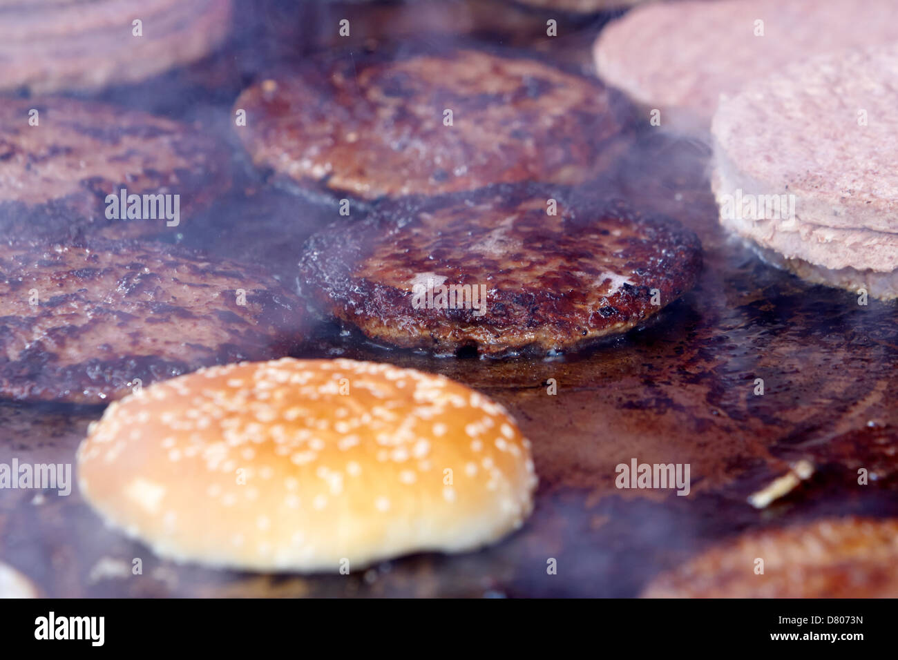 raw and cooked processed hamburgers on a commercial flat grill at an outdoor event Stock Photo