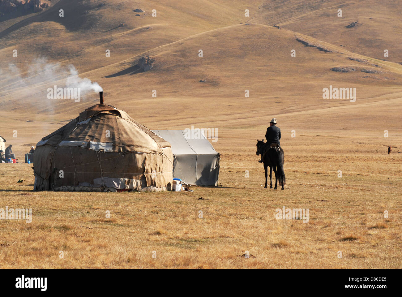 Kyrgyz man riding a black horse approaches a yurt in the highland pastures at the Song Kul lake. Naryn region, Kyrgyzstan Stock Photo
