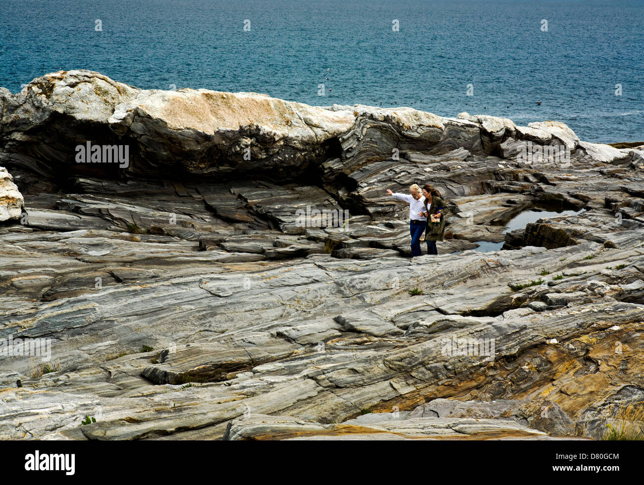 Man and woman walking close together in conversation along a towering rock formation on the Maine coast. Stock Photo