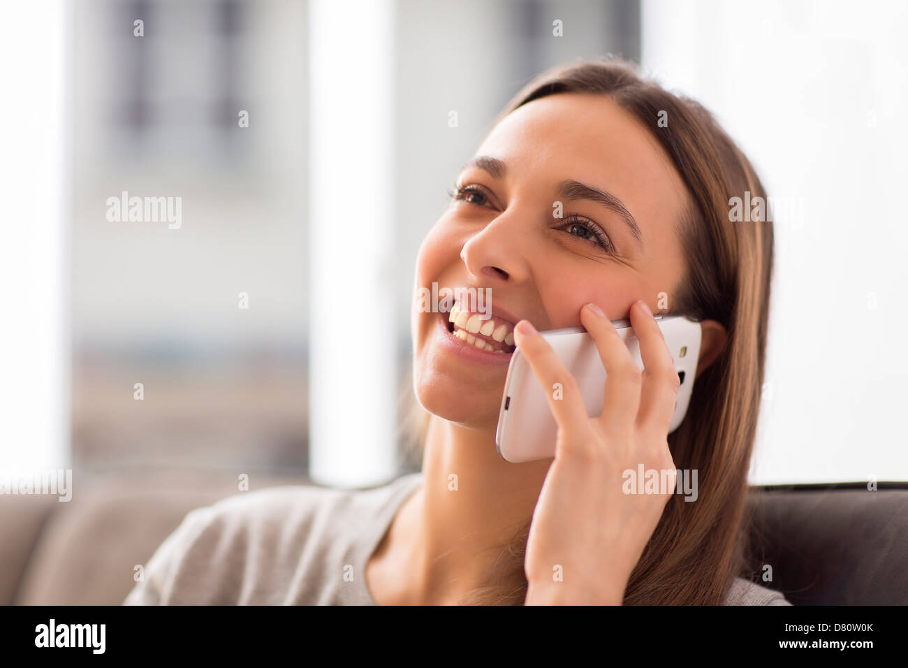 Pretty young female using white mobile phone at home smiling Stock Photo
