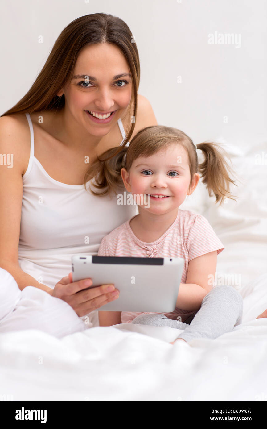 Portrait of a little girl playing tablet with her mom in the white bedroom Stock Photo