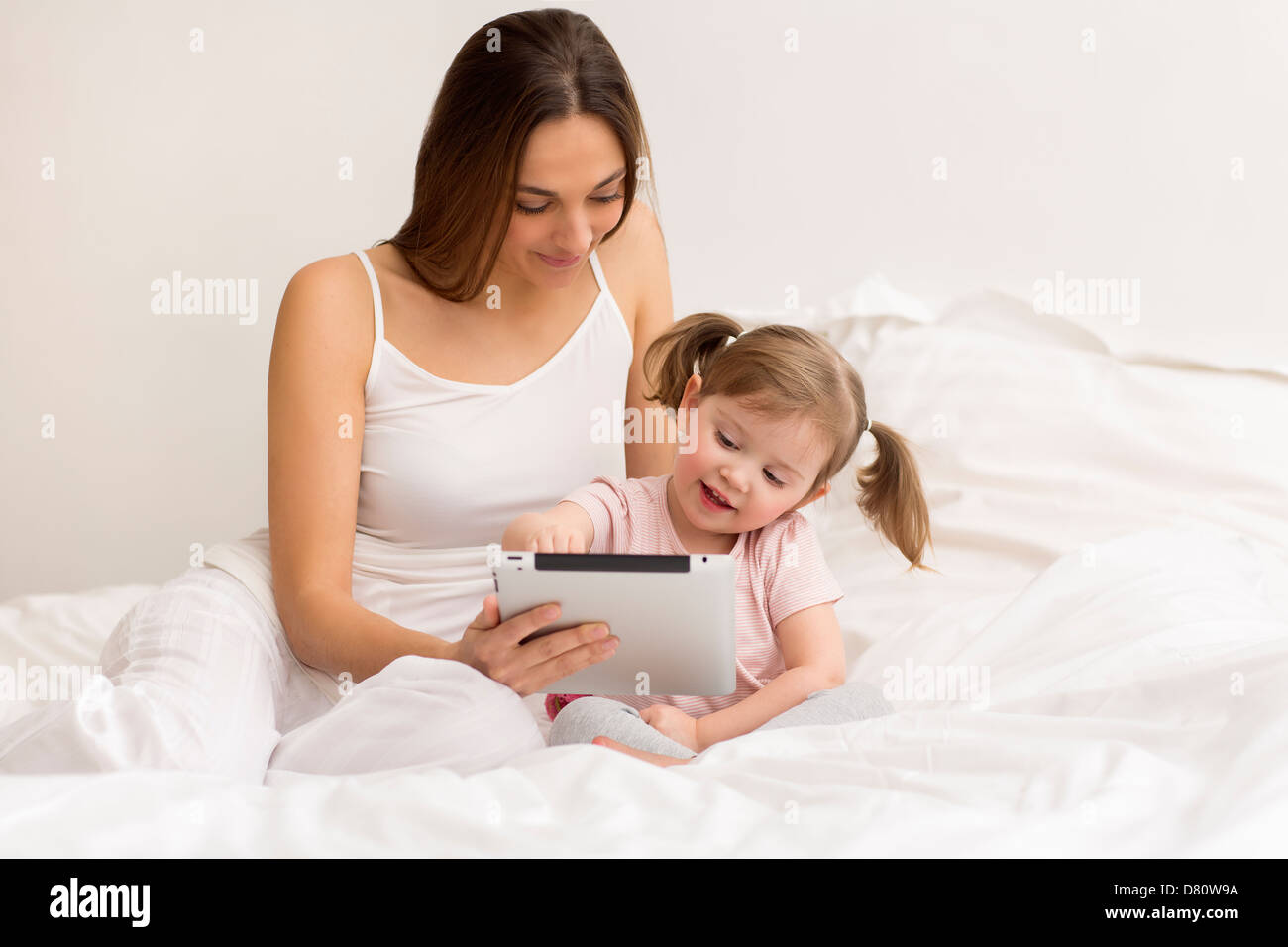 little girl playing tablet with her mom in the white bedroom Stock Photo