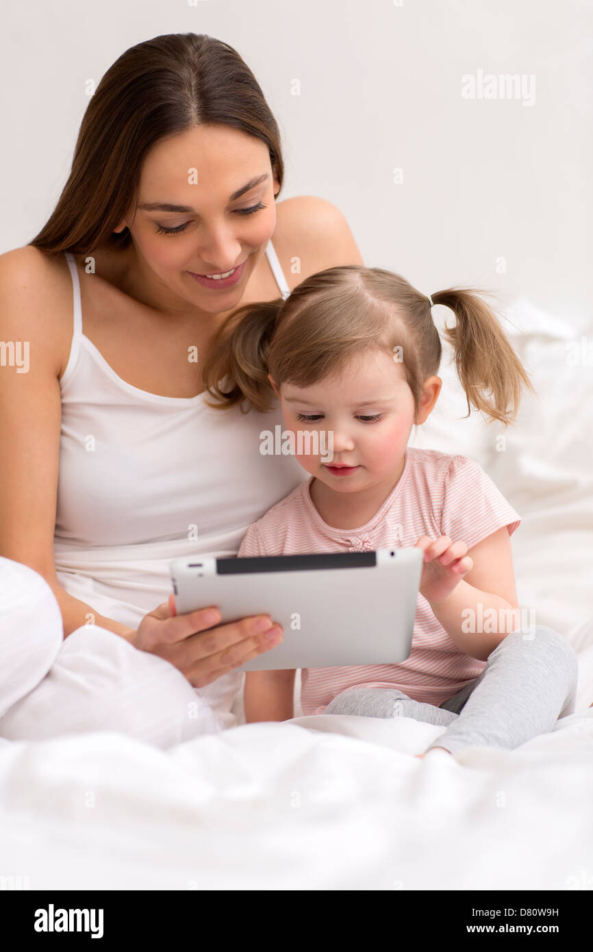 little girl playing tablet with her mom in the white bedroom Stock Photo