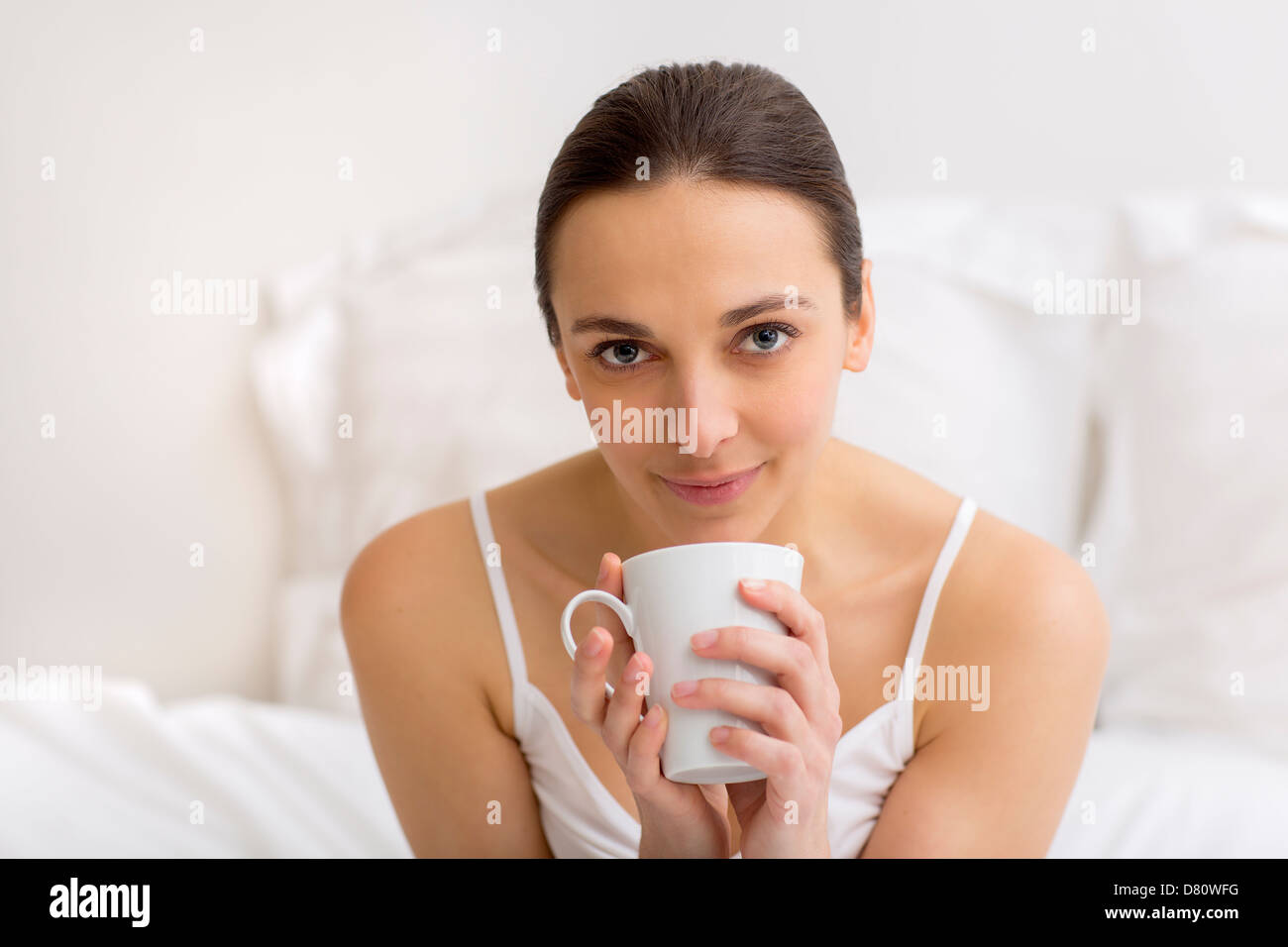 Portrait woman enjoying tea in white bedroom Stock Photo