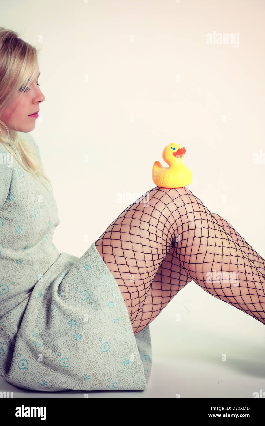 a blond girl with a turqouise dress is sitting with a rubber duck on her knees Stock Photo