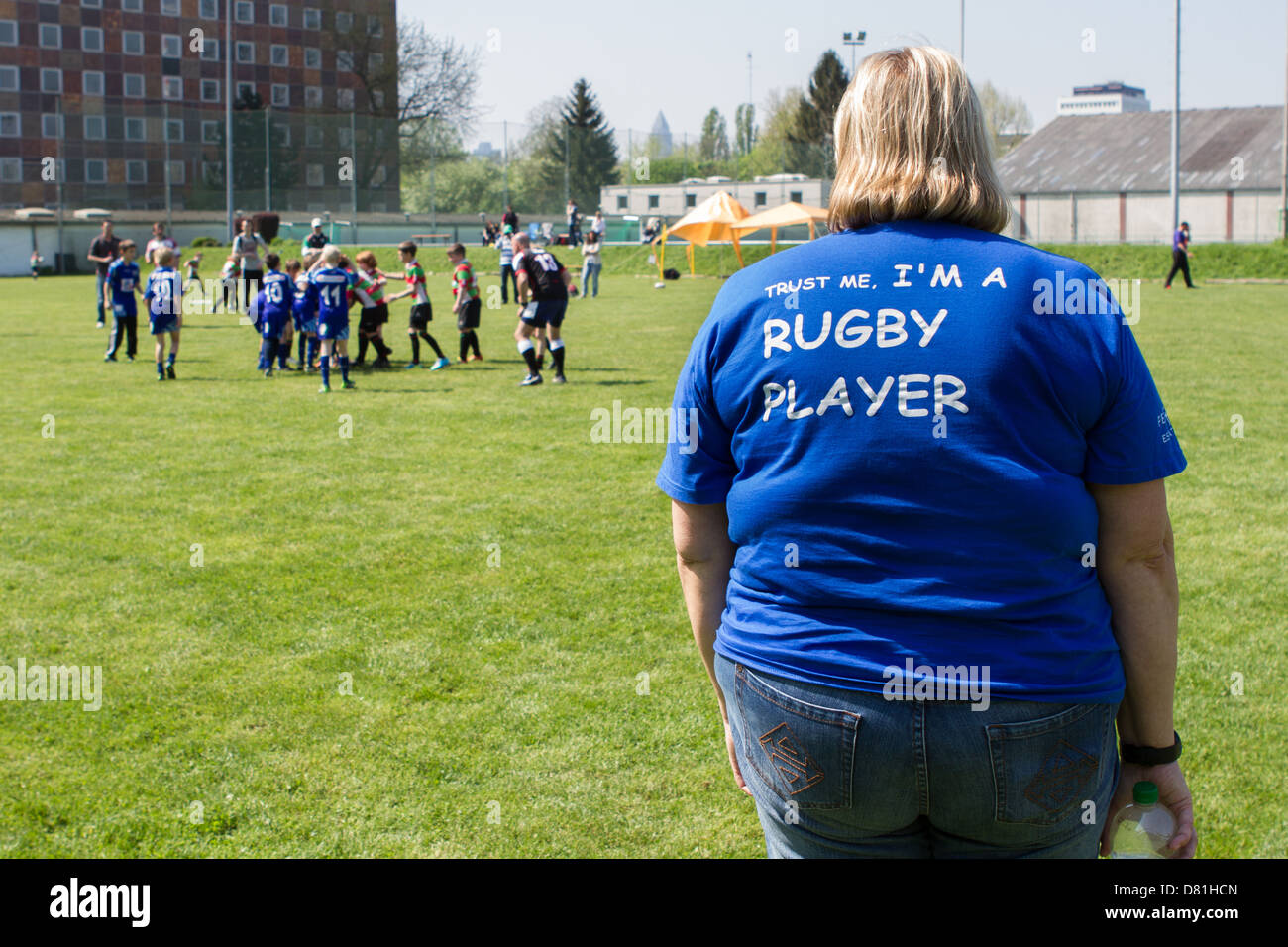 A woman with a 'Trust me, I'm a rugby player' t-shirt watches a children's rugby match Stock Photo