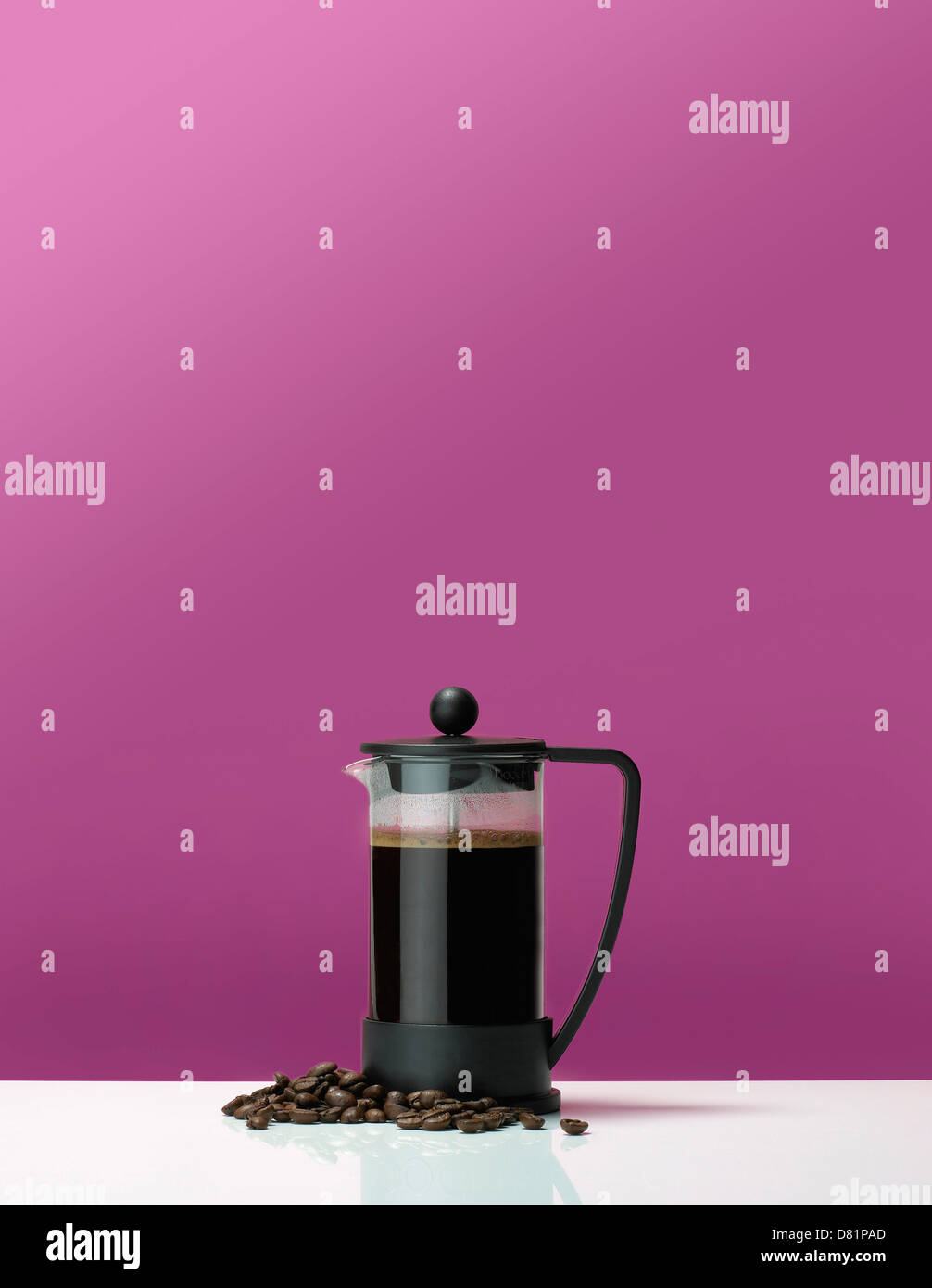Coffee pot cafetiere on a table with coffee beans against a pink background Stock Photo