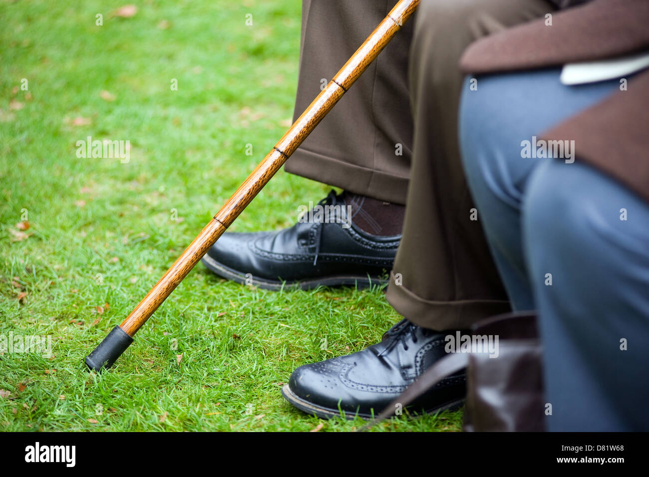 An old man sitting with a walking stick in his hand Stock Photo