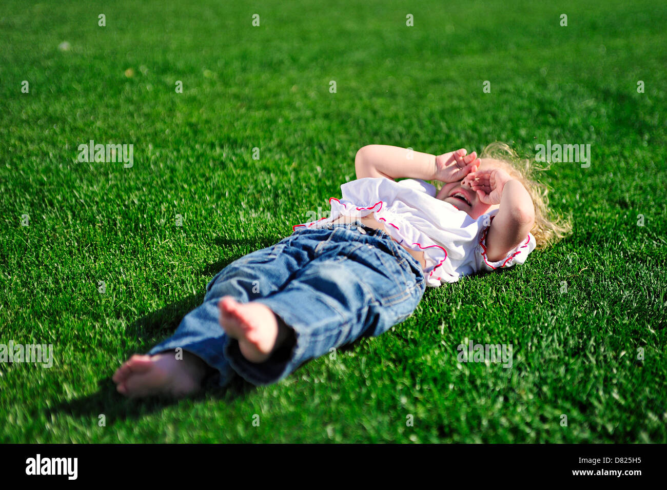 Cute little girl laying on the green grass in the park Stock Photo - Alamy