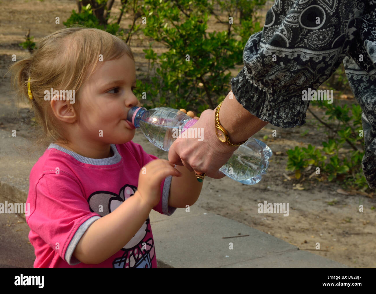 2 year old little child drinking water in a park Stock Photo