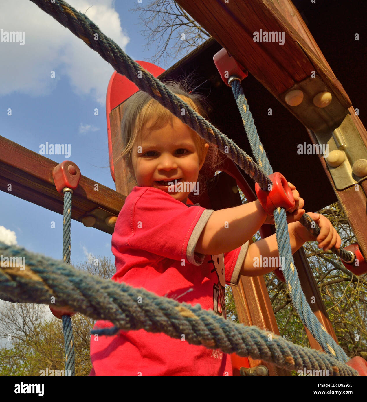 2 year old girl walk on jungle gym at playground smiling Stock Photo