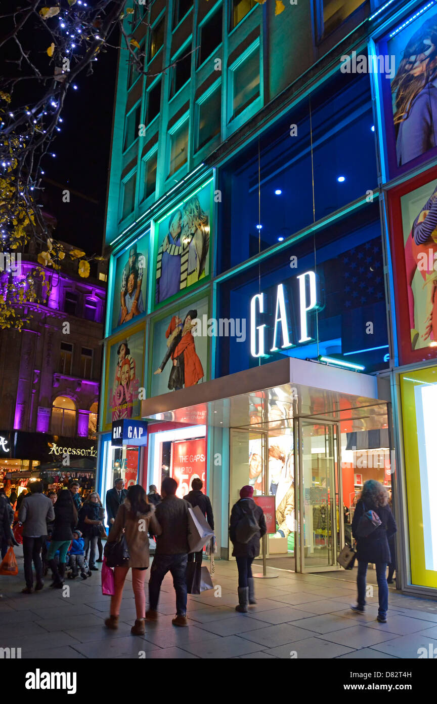 Shoppers outside Gap clothing fashion store shop front window with coloured illuminations on Oxford Street West End of London England UK Stock Photo