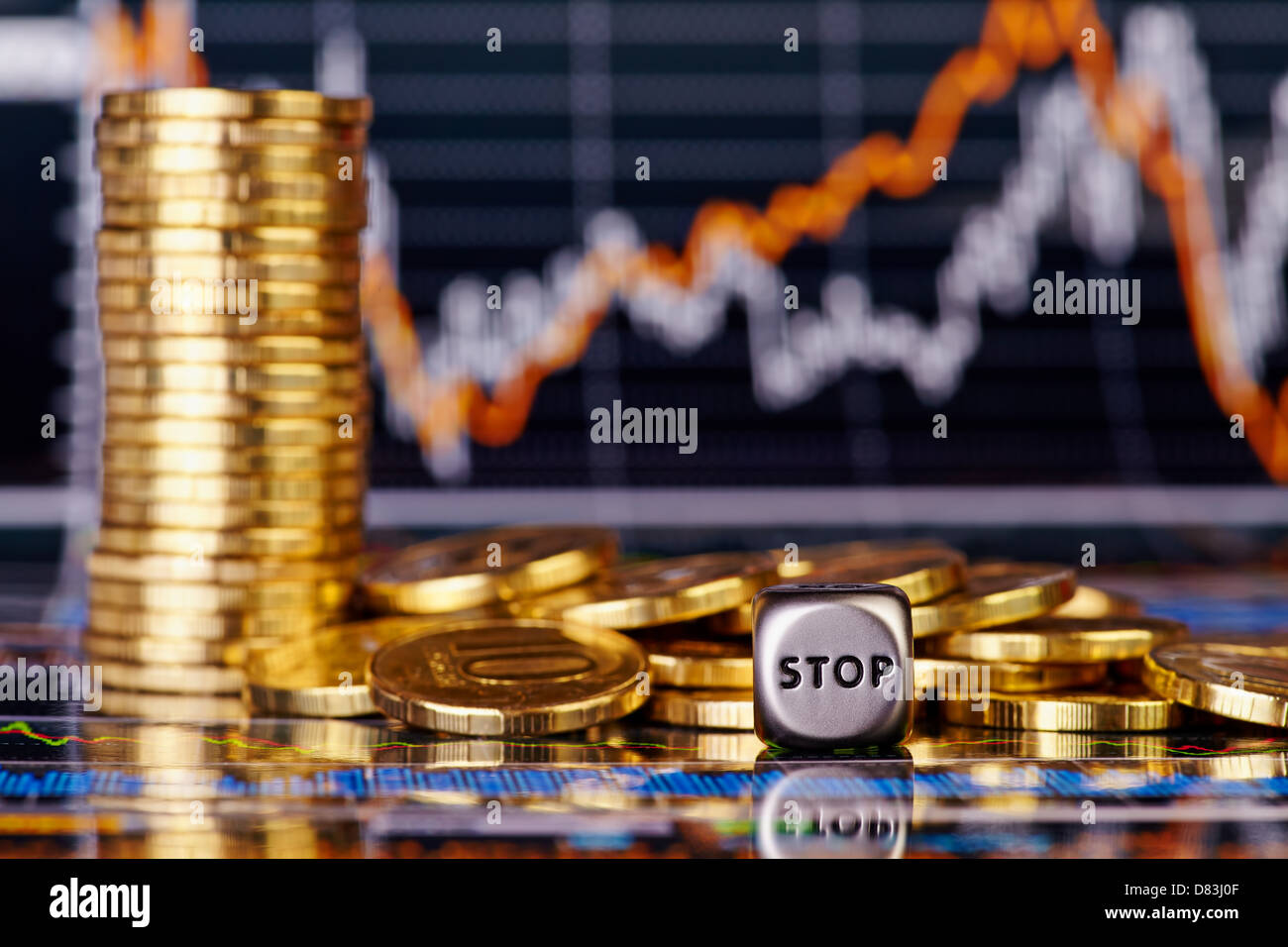 Dices cube with the word STOP golden coins. Financial stock charts as background. Selective focus Stock Photo