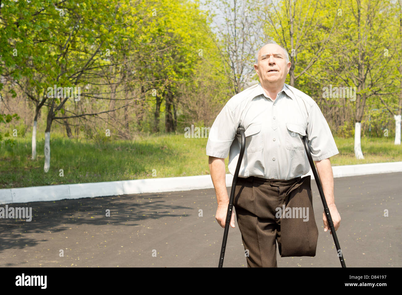 Elderly male amputee balanced on crutches in a rural street with his trousers pinned up to reveal his stump Stock Photo