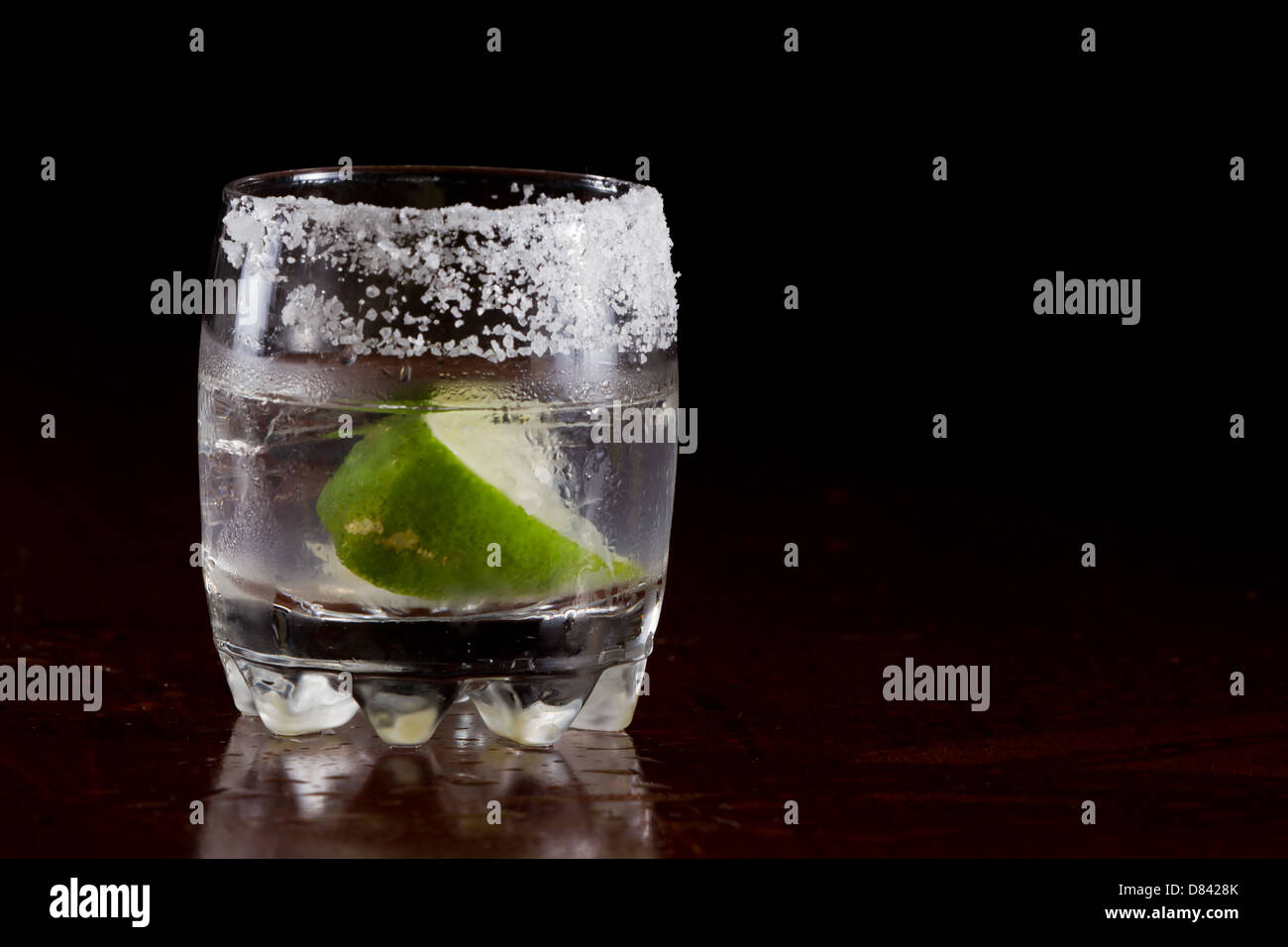 silver tequila shot served on the rocks in a small glass with a lime wedge and salt on the rim Stock Photo