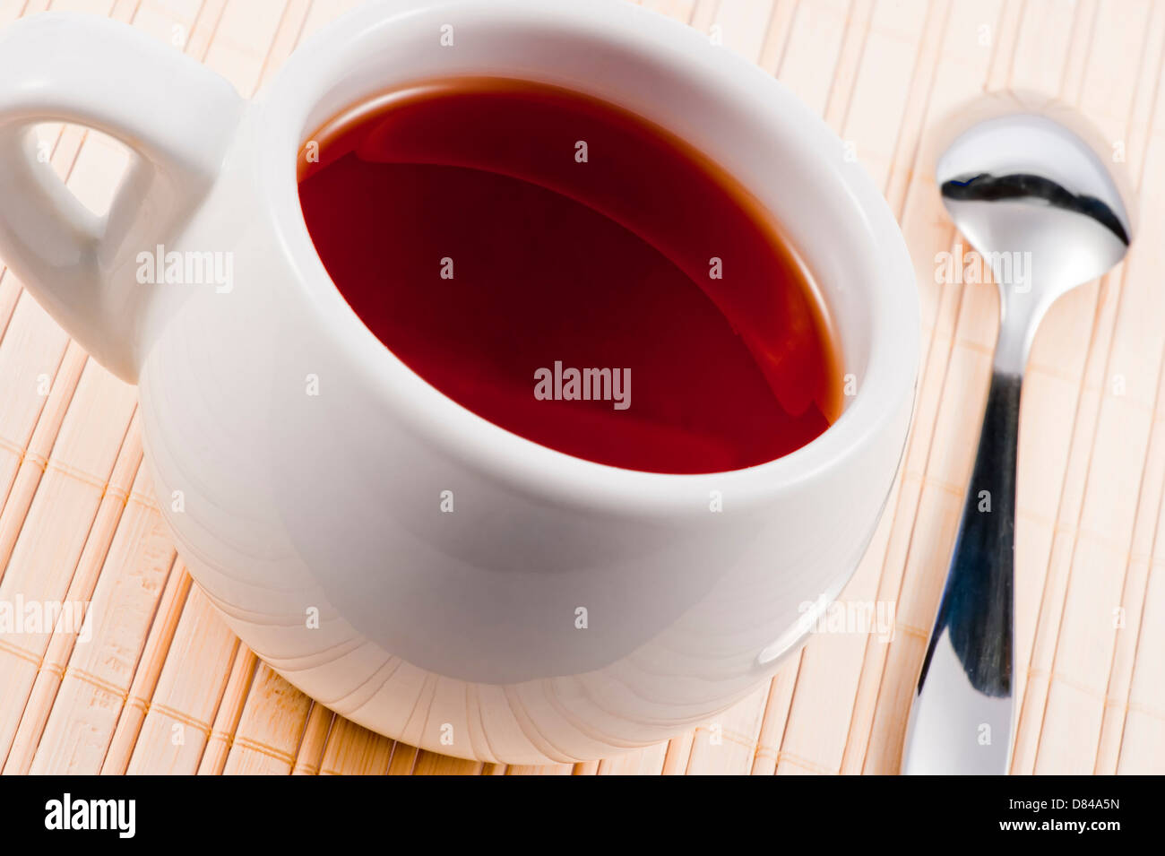White cup with fresh tea on wooden mat. Stock Photo
