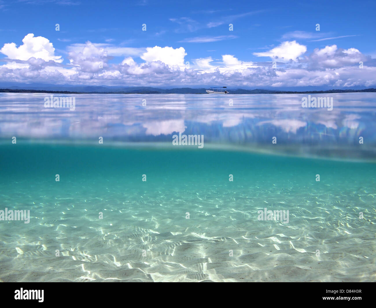 Above and below water in the Caribbean sea with clouds reflected on water surface and sandy seabed underwater Stock Photo