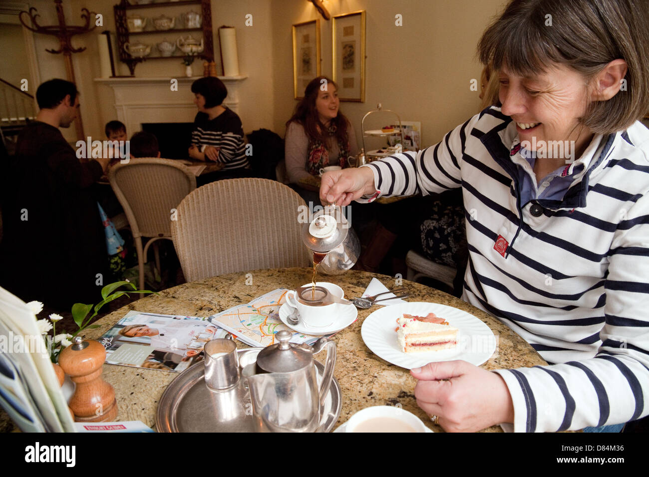 A woman pouring afternoon tea and eating cake, Little Bettys Cafe Tea Rooms, York UK Stock Photo