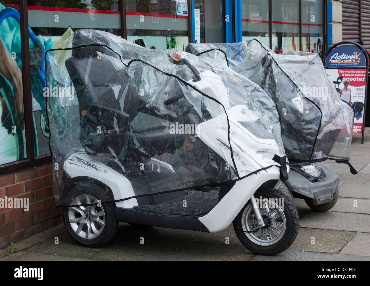 Mobility Scooters with rain covers outside shop. England, UK Stock Photo