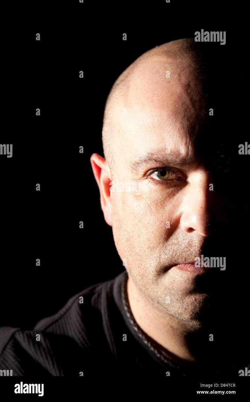 Bald headed man looking straight at the camera with half his face in deep shadow for a more dramatic image. Stock Photo