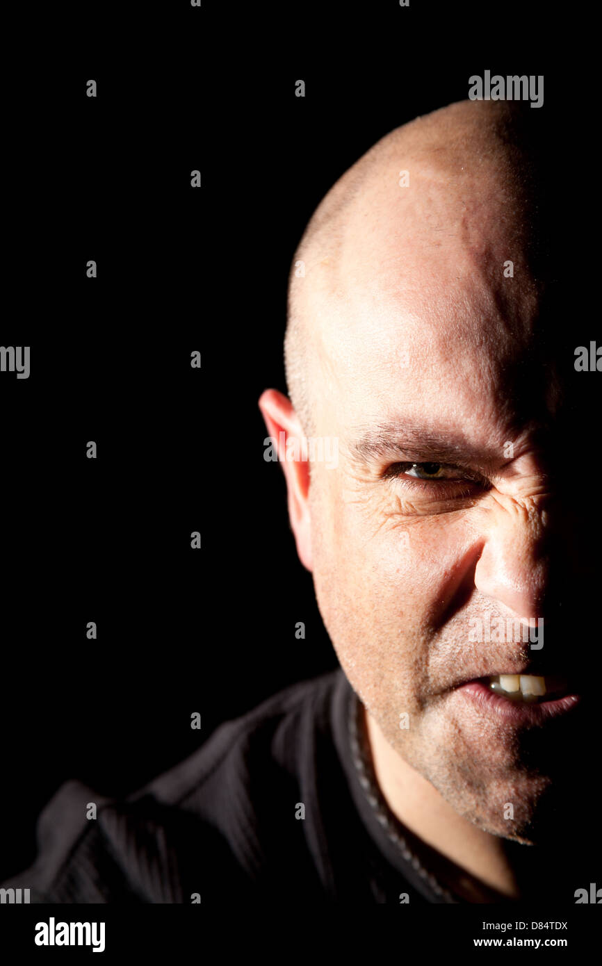 Distraught bald man with half face in deep shadow against a black background. Stock Photo
