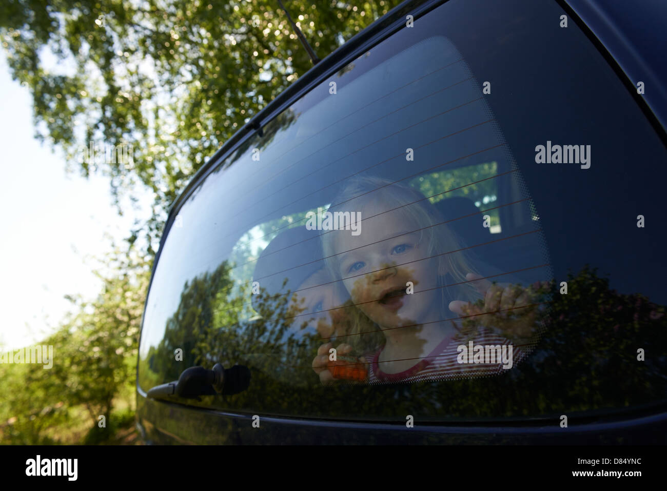 Child toddler girl in the car looking out through rear car door window Stock Photo