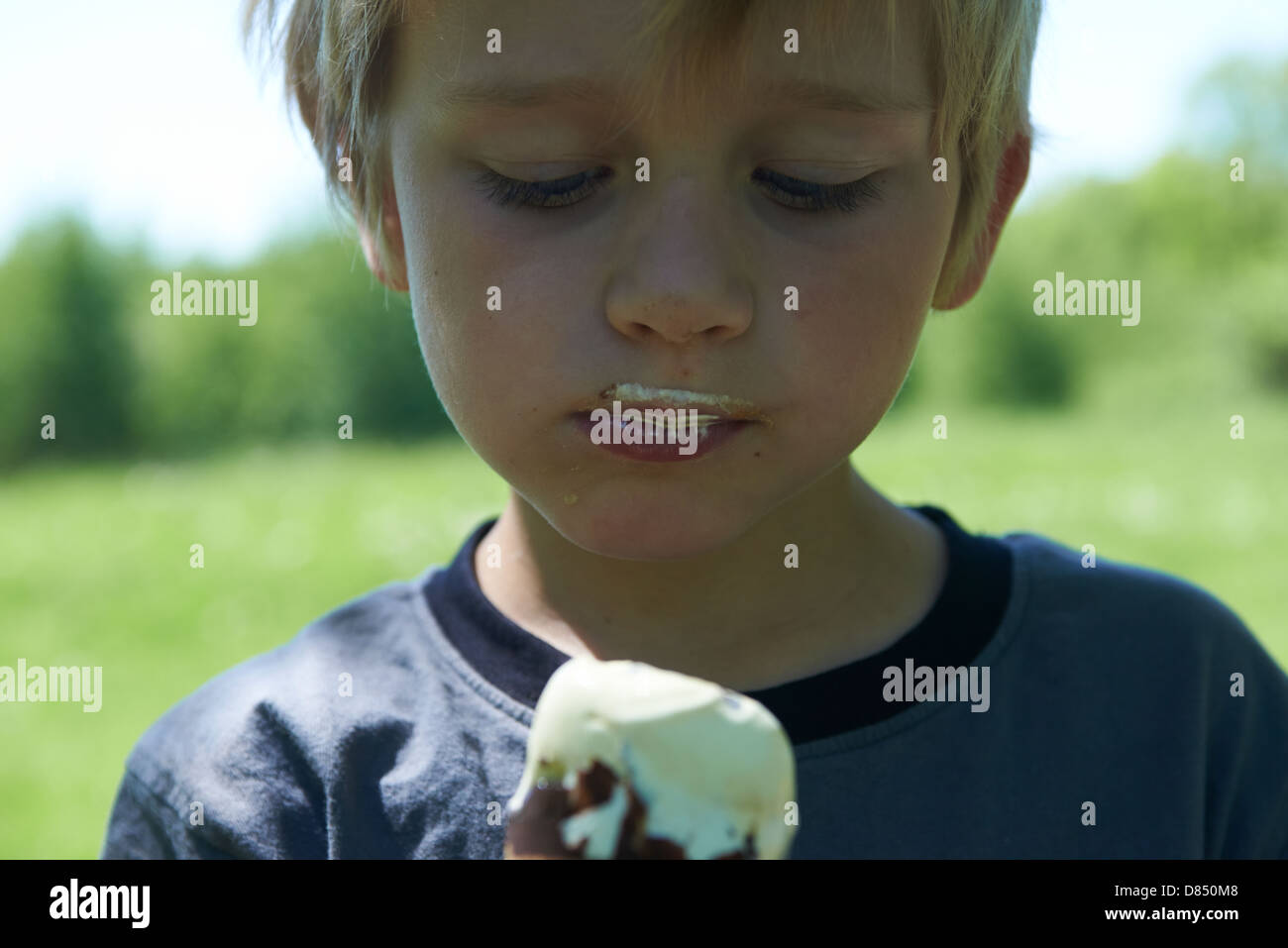 Blond child 68 year old boy holds and eating ice cream summertime