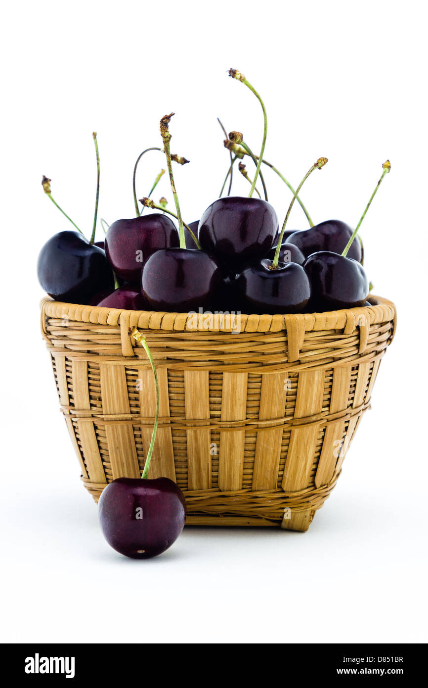 Black cherries sitting in a basket isolated on a white background. Stock Photo